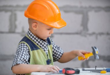 Elinde çekiç tutan kasklı bir çocuk. İnşaat alanında oyuncak aletlerine yardım eden küçük bir çocuk. İnşaat aletleri olan çocuklar. Çocuk inşaatçısı ve tamircisi.