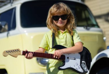 Sarı kıvırcık saçlı, bej sarısı arka planda gitar çalan komik çocuk. Gitar çalan komik hippi müzisyen çocuk.