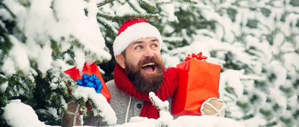 冬の雪の背景にギフトボックスを屋外で興奮したサンタ クリスマスの帽子の男は屋外を提示します 雪の冬の背景 雪の中でプレゼントを運ぶサンタ屋外 — ストック写真