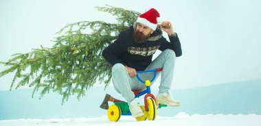 Bisikletli komik bir adam Noel ağacını önemsiyor. Kışın arka planda kardan adam. Kış bayrağı için kardan adam. Çocuk bisikleti üstünde komik bir baba Noel ağacı tut