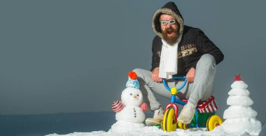 Çocuk bisikleti süren çılgın kış adamı. Kışın arka planda kardan adam. Kış bayrağı için kardan adam. Dışarıda bisiklete binen komik baba.