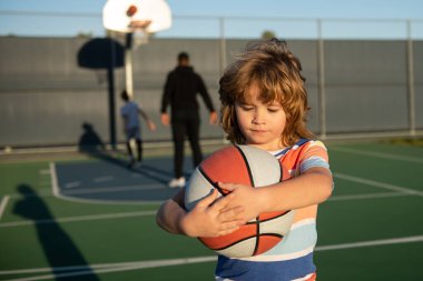 Sevimli gülümseyen çocuk basketbol oynuyor. Aktif çocuklar basket topuyla dışarıda oyun oynuyorlar.