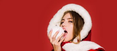Güzel bir kadının yakın plan portresi, kışın Noel tatilini kutluyor. Kırmızı arka planda izole edilmiş Noel baloları var. Genç ve güzel bir kız Noel balosuyla
