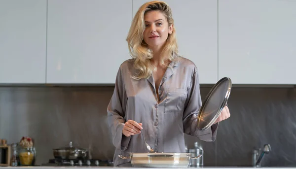 家事をしながら鍋料理をする女性 家事の概念 セクシーな主婦はキッチンで朝食を持っています 家庭生活 朝台所に立つ官能的な女性 — ストック写真