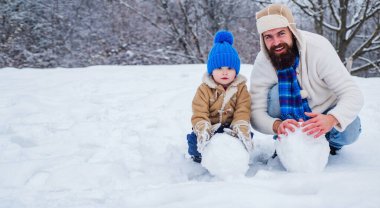 Tatlı küçük çocuk ve karlı arazide mutlu bir baba. Baba ve oğul karda kartopu yapıyorlar. Baba ve çocuk kışın açık havada kartopu oynuyorlar.