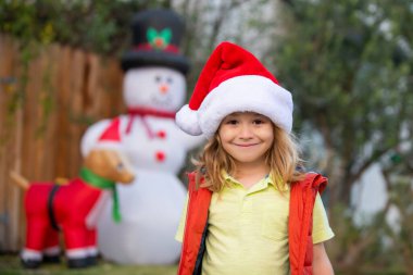 Mutlu yıllar ve mutlu Noeller. Noel Baba şapkalı çocuk evin arka bahçesini duyuyor. Noel akşamı