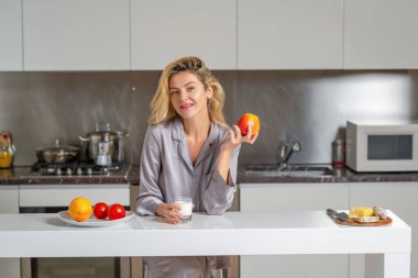 Kahvaltı için elma ve süt. Güzel bir kadın, sıcacık bir mutfakta sağlıklı yiyeceklerle kahvaltı eder.