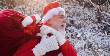 Bir çuval dolusu Noel Baba dışarıda hediyelerle bekliyor. Noel Baba kar parkında yürüyor