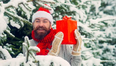 Mutlu Noel Baba 'nın dışarıda hediye kutusuyla portresi. Noel hediyeli mutlu adam dışarıda. Karlı kış arkaplanı. Mutlu Noel Baba 'nın dışarıda kar yağarken çekilmiş fotoğrafı. Elinde hediyeler var.