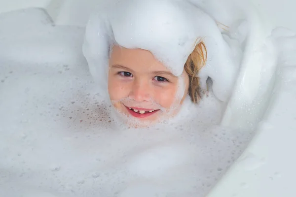 Kids face in foam. Kid having fun in the bath with bubbles. Happy child enjoying bath time. Little boy smiling in the bath with soap foam. Child bathes in a bath with foam