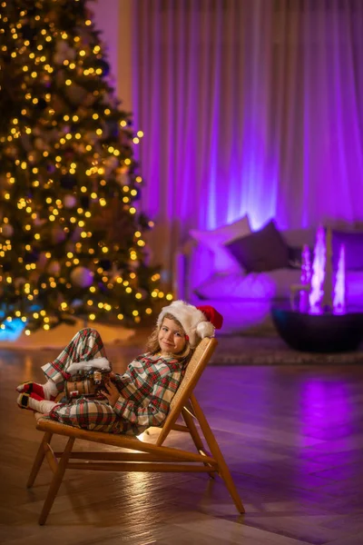 子供でサンタ帽子の前に夜のクリスマスツリーホーム背景上のクリスマスイブ — ストック写真