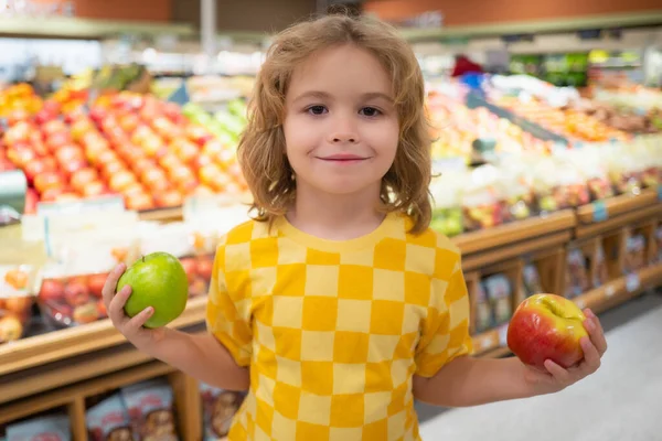 Child hold apple fruits at grocery store. Kid is choosing fresh vegetables and fruits in the store. Child buying food in grocery supermarket. Buying in grocery store. Groceries in the supermarket