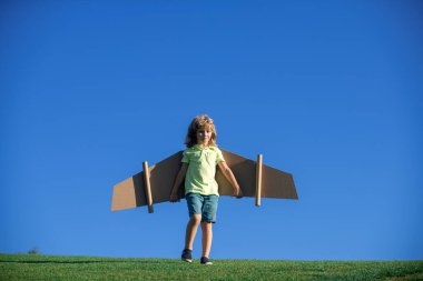 Komik çocuk dışarıda uçak kanatlarıyla oynuyor. Pilotçuluk oynayıp pilot olmanın hayalini kuran sevimli çocuk. Dışarıda kağıt kanatlarla eğlenen bir çocuk. Yaz tatili ve çocukların seyahat konsepti