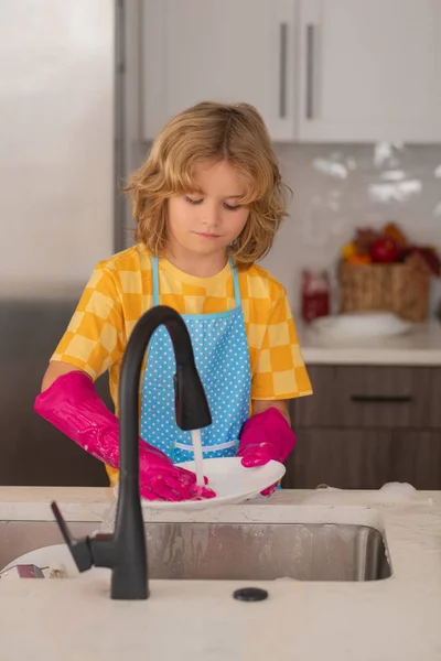 Cleaning at home. Kid washing dishes in the kitchen interior. Child helping with housework. Housekeeping and home cleaning concept. Child use duster and gloves for cleaning