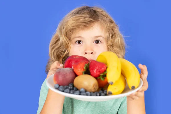 Funny child hold plate with fruits. Funny child eating fresh fruit. Child eating fresh fruit. Kid with fruits and vegetables. Healthy food