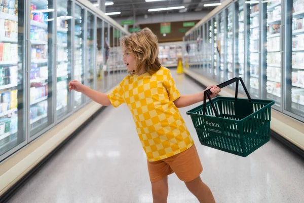 Child with shopping basket at grocery store. Funny cute child on shopping in supermarket. Grocery store. Grocery shopping, healthy lifestyle concept
