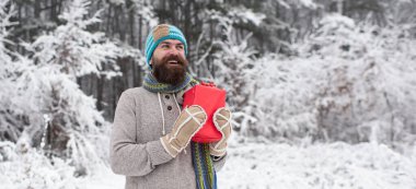 Kışın açık havada hediyeli mutlu bir adam. Örgü şapkalı ve kışlık kazaklı hippi dışarıda eğleniyor. Kış karlı doğada gülen adam.