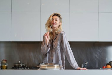 Ot pişiren, ev işi yapan bir kadın. Oda servisi konsepti. Mutfakta yemek hazırlayan seksi kadın. Ev mutfağında seksi pijama giyen bir kadın kahvaltı hazırlıyor.