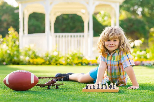 Dream kids and childhood concept. Early development. Boy thinking about chess in summer park. The concept of learning and growing children. Outdoor game, kids hobby and lifestyle