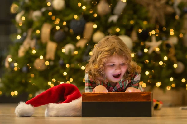 Surprise kid opening Christmas present gift box. Kid boy near christmas tree at home