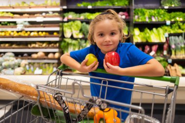 Marketteki elma meyveli çocuk. Çocuklarla alışveriş. Çocuk süpermarketten meyve alıyor. Küçük çocuk marketten taze sebze alır. Çocuk sebze seçiyor. Sağlıklı yemek.