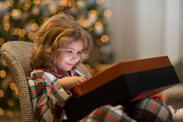 Surprise kid opening Christmas present gift box. Little kid celebrating Christmas or New Year near Christmas tree at home