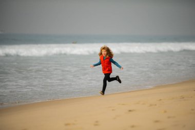 Sportif çocuk doğada koşuyor. Deniz kıyısına yakın sularda koşan bir çocuk. Küçük bir koşucu egzersizi. Çocuk deniz kıyısında koşuyor. Çocukların geri kalanı yaz tatilinde.