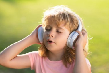 Şarkı söyleyen çocuklar. Kulaklıklı genç çocuk müzik dinliyor, açık havada gözleriyle favori müziğin tadını çıkarıyor.