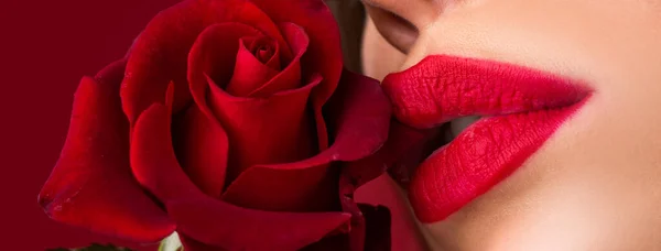 Lips with lipstick closeup. Woman with red rose, macro, on red background. Beautiful woman lips with rose. Close-up beautiful female lips with bright red makeup