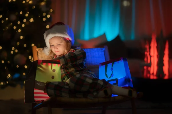 Kid with present gift with magic light. Lighting present gift bag. Kid in Christmas pajama enjoying holiday evening at home