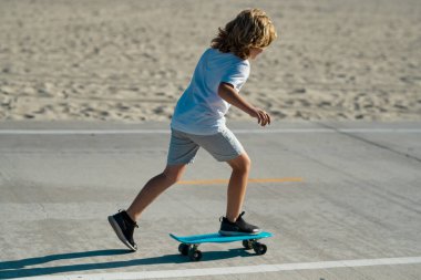 Çocuk kaykaycı sokakta kaykaya biniyor. Yaz şehrinde bir çocuk. Küçük bir çocuk, parkta ilk kez kaykay süren küçük bir çocuk, kaykay yapmaya çalışıyor.