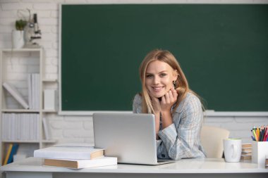 Sınıfta dizüstü bilgisayarla çalışan bir üniversite öğrencisi sınava hazırlanıyor. Dizüstü bilgisayar kullanan yaratıcı, gülümseyen kız öğrenci.