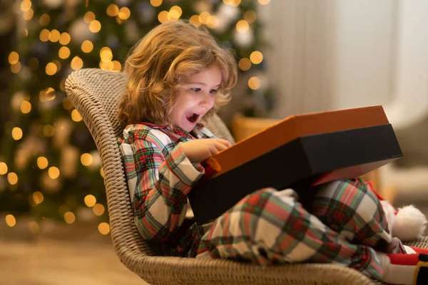 Surprise kid opening Christmas magic presents. Happy excited child open Christmas gift near christmas tree at home