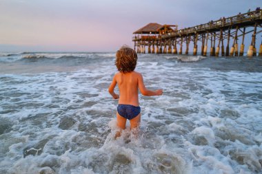 Yaz tatilinde tropik plaj adasında açık havada oynayan bir çocuk. Denizde oynayan mutlu çocuk. Arka planında beyaz büyük dalgalar olan mavi okyanus.