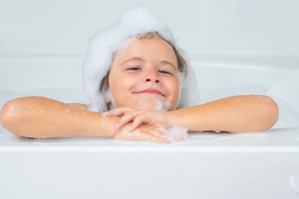 Little child in a bath tub. Washing in bath. Kid with soap suds on hair taking bath. Closeup portrait of smiling kid, health care and kids hygiene. Kids face in bath tub with foam close up