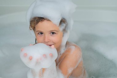 Çocuklar banyo yapıyor. Çocuk köpüklerle banyoda eğleniyor. Mutlu çocuk banyonun tadını çıkarıyor. Küçük çocuk sabun köpüğüyle banyoda gülümsüyor. Çocuk köpükle banyo yapar.