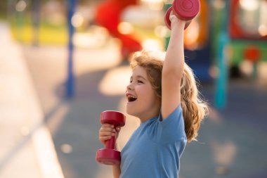 Çocuklar dışarıda oyun alanında spor yapıyor. Çocuklarla boş zamanlarında spor aktiviteleri. Sportif çocuk, elinde dambıl tutuyor.