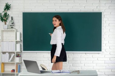 Genç, kendinden emin ve çekici bir kız öğrencinin portresi. Elinde tebeşirle okul arkaplanında duruyor.