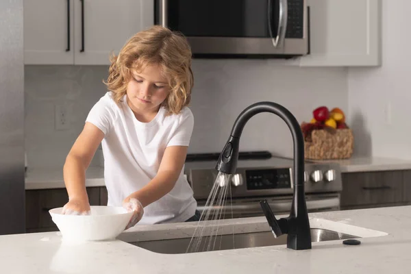 Child with sponge with dish washing liquid is doing the dishes at home kitchen by using wash sponge and dishwashing. Cleaning dishware kitchen sink sponge washing dish