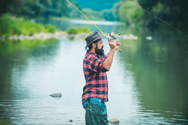 Young man fishing. Fisherman with rod, spinning reel on river bank. Man catching fish, pulling rod while fishing on lake. Wild nature. Fishing hobby and spring weekend
