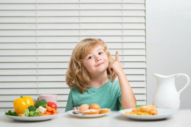Okul çocuğu okuldan önce kahvaltı yapıyor. Küçük bir çocuğun portresi. Mutfaktaki masada oturuyor. Lezzetli, besleyici bir kahvaltı yapıyor.