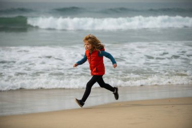 Sportif çocuk doğada koşuyor. Çocuk deniz kenarında koşuyor. Sahilde koşan çocuklar. Yaz tatili. Kumsalda oynayan mutlu çocuk. Mutlu çocukluk