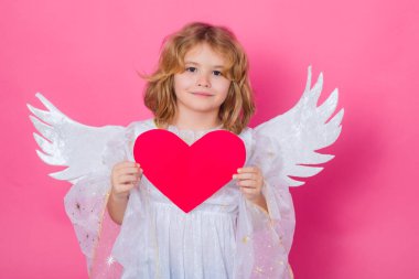 Kalbi olan melek çocuk. Sevgililer Günü. Pembe stüdyo arka planında melek kanatları olan sarışın şirin çocuk. Mutlu melek çocuk