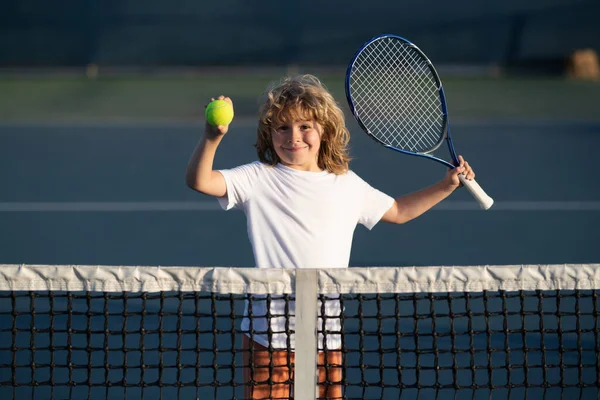 Child playing tennis on outdoor court. Kid with tennis racket and tennis ball playing on tennis court