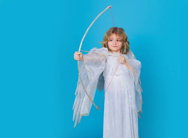 Cupids arrow hit right in heart, arrow of love. Angel with bow and arrow. Cute angel kid, studio portrait. Blonde curly little angel child with angels wings, isolated background