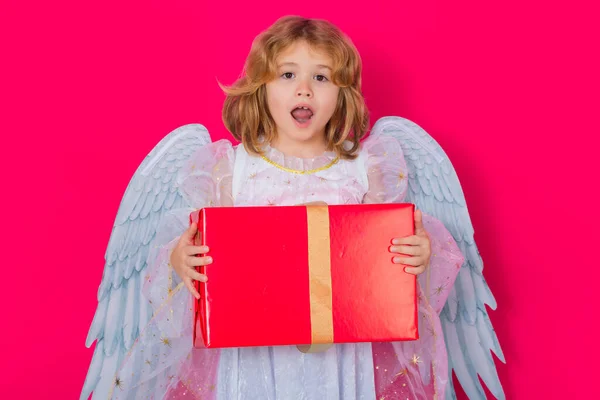 Cute child angel with gift box present. Valentine angel. Little cupid child. Kid angel with angels wings, isolated on pink studio background. Valentines day gift card
