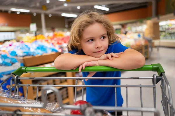 Kid with shopping cart at grocery store. Kid is choosing fresh vegetables and fruits in the store. Child buying food in grocery supermarket. Buying in grocery store. Groceries in the supermarket