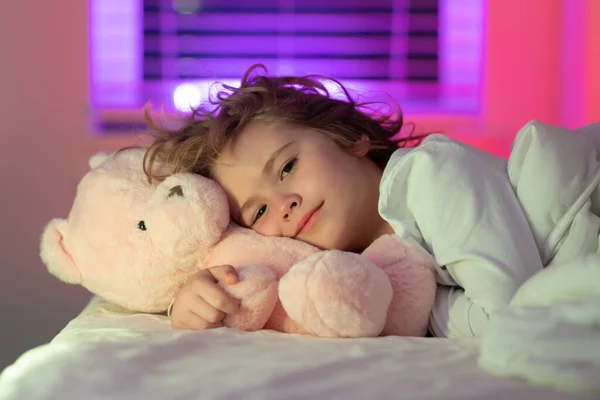 Kid in bed with toy teddy bear. Nap and sleep time. Favorite toy for sleep. Bedding and sleepwear for children