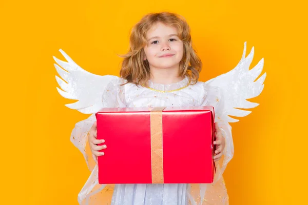 Cute blonde kid angel with gift box present. Valentines day. Little cupid angel child with wings. Studio portrait of angelic kid
