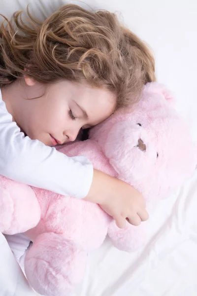 Morning sleep. Adorable kid sleeps with a toy teddy bear in bed. Sleeping child